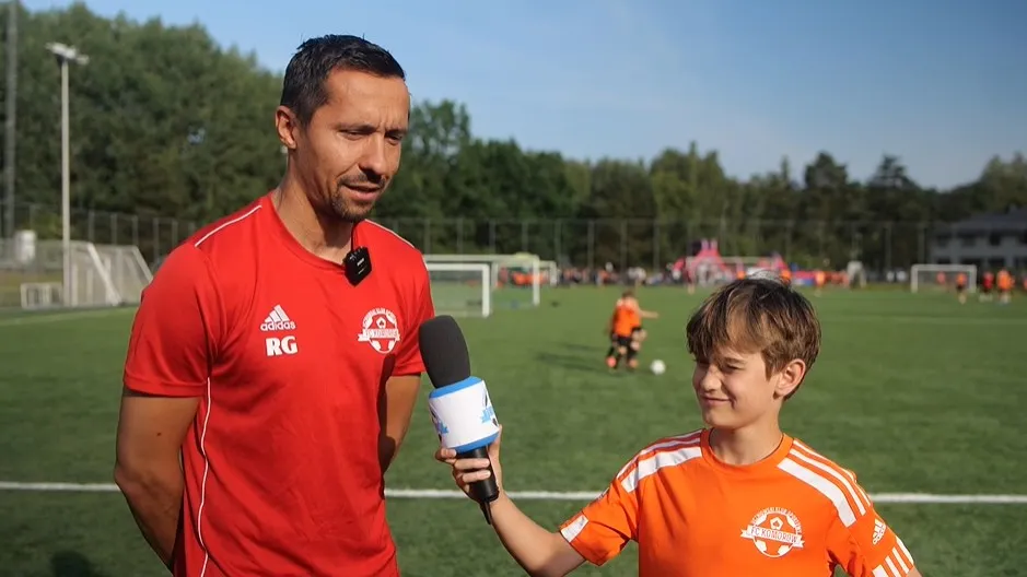Młody zawodnik z mikrofonem na boisku piłkarskim, kadr z wywiadu dla FC Komorów